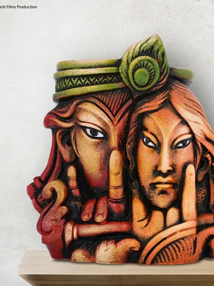 A close-up shot of a terracotta Radha-Krishna showpiece. The lighting is carefully controlled to highlight the intricate details, texture, and colors of the handcrafted item.