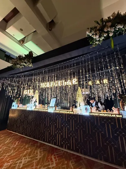 Sophistication at its finest. This Art Deco inspired bar combines a sleek, patterned facade with elegant crystal curtain backdrops and bold, illuminated 'GIN MOLECULAR BAR' lettering, perfect for a chic and upscale cocktail evening.