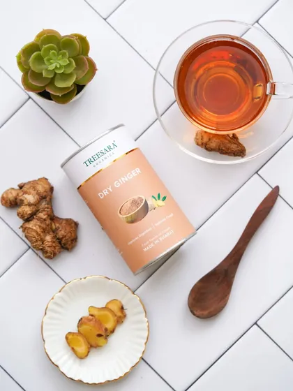 A top-down flat-lay of dry ginger powder, styled with fresh ginger, a cup of tea, and a succulent on a tiled background.