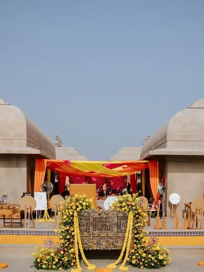 A wide shot of the Haldi venue, showing the vibrant drapes and marigold decorations against the traditional architecture of the Fairmont Jaipur.