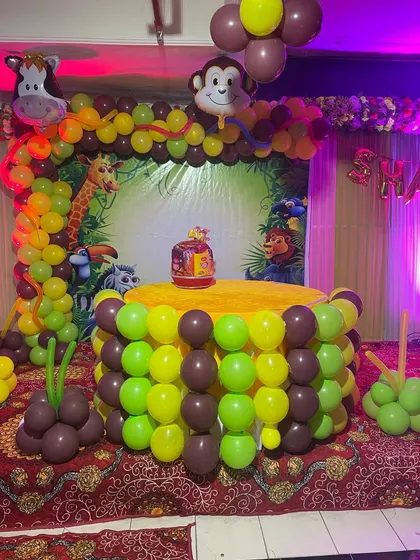 A closer look at the jungle-themed birthday party setup. You can see the animal-print backdrop, a balloon arch with monkey and cow foil balloons, and a cake table surrounded by green and brown balloons.