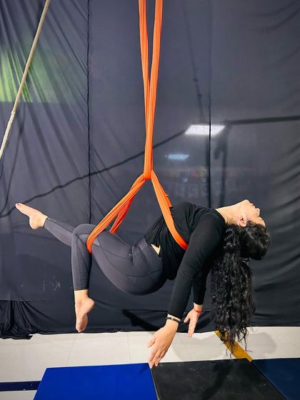 A student rests gracefully in the silk hammock, a pose that builds core engagement while allowing for a moment of calm suspension.