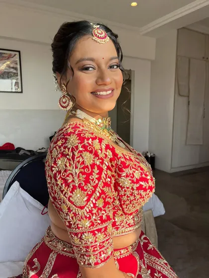 A duplicate of a previous image, showing a happy bride in her red lehenga. The makeup is fresh, radiant, and perfectly suited to her style.