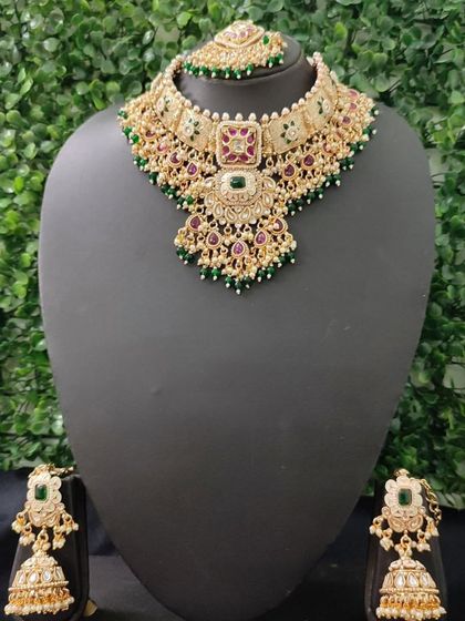 A full kundan bridal set with a choker, matching earrings, and maang tikka, featuring green and maroon stones.