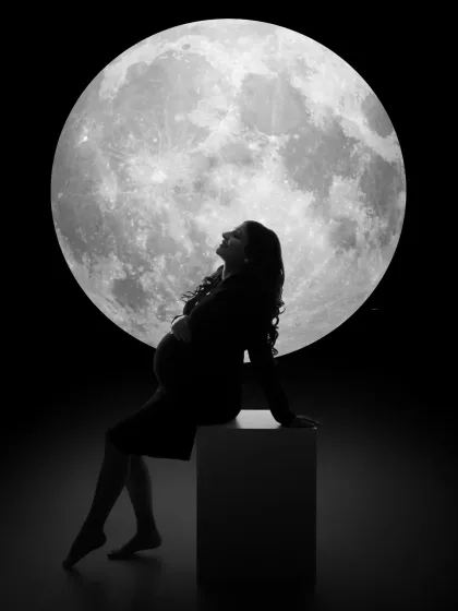 A timeless silhouette against a full moon. We use creative lighting to craft dramatic and emotional monochrome portraits. This image beautifully captures the iconic shape of the baby bump, creating a powerful and artistic memory of the pregnancy journey.