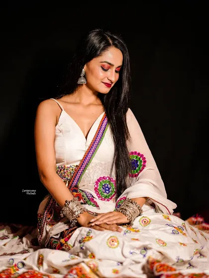A gentle and contemplative pose, with the model looking down at her hands, showcasing the intricate details of her Navratri outfit and jewelry.