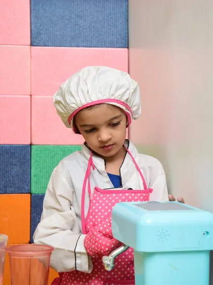 A little chef in a full uniform, including a hat and apron, getting serious about her pretend cooking.