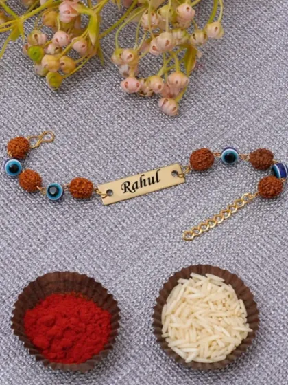 A close-up of our personalized Rudraksha and evil eye name rakhi. We engrave your brother's name on the golden plate, creating a meaningful and protective thread for Raksha Bandhan.