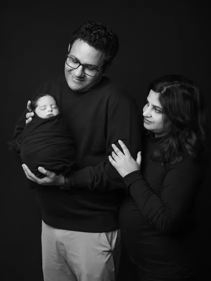 A classic studio portrait of a new family. The parents' admiring gaze towards their sleeping baby, wrapped snugly, tells a story of love and wonder.