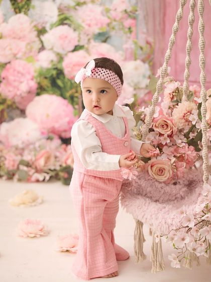 Standing tall by the floral swing. This shot captures a proud milestone moment against a beautiful backdrop of pink flowers.