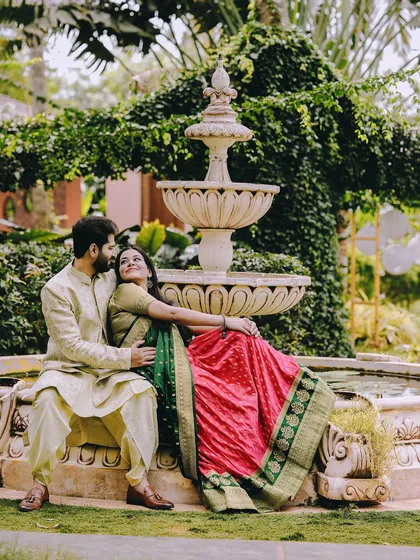 A regal pre-wedding portrait of a couple in rich, traditional Indian outfits, relaxing by an ornate garden fountain, creating a timeless and romantic image.