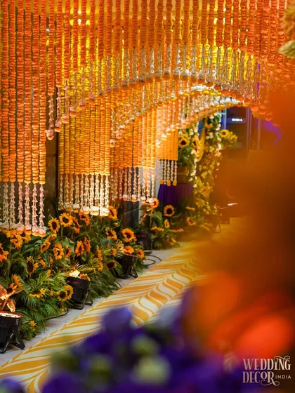 An artful shot of the marigold tunnel entrance, with a blurred foreground of purple flowers creating a beautiful color contrast and a sense of depth.