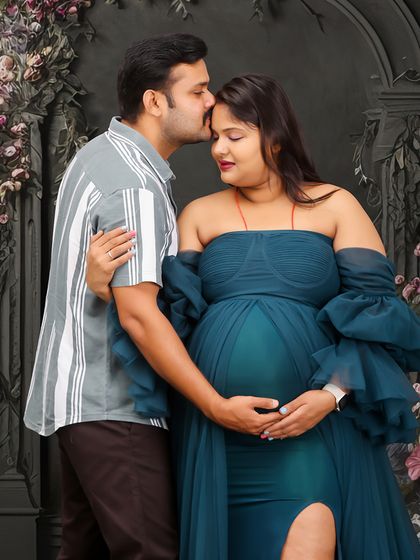 A close-up, emotional moment during a studio maternity session. The partner's gentle kiss on the forehead conveys love and support against a beautiful floral backdrop.