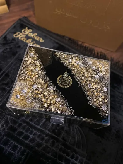 A top-down view of my trending black and gold Islamic gift set. This luxurious collection includes a personalized prayer mat, a resin Quran box, and a matching Quran holder, all heavily embellished for a grand look.