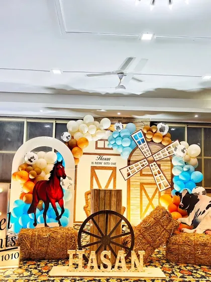 A unique cowboy and farm theme birthday decoration. This setup creates a rustic feel with hay bales, a wooden fence, a barn-style backdrop, and cutouts of a horse and cow, personalized with the birthday boy's name.