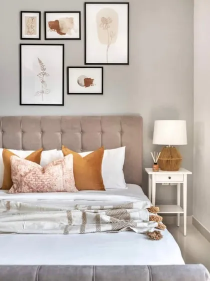 A beautifully styled bedroom featuring a tufted headboard and a curated gallery wall. The mix of warm terracotta pillows and soft throws adds a touch of color and comfort to the neutral space.