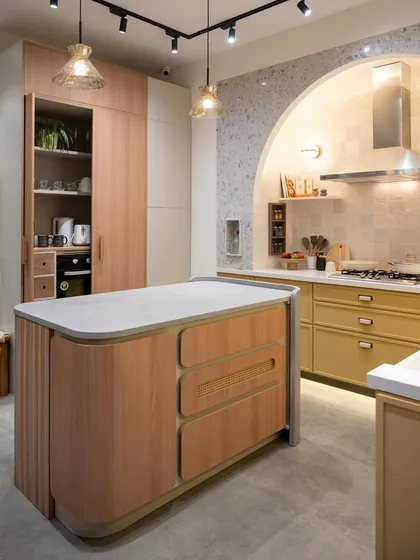 A wide view of this warm, contemporary kitchen, showing the curved island, the tall pantry unit, and the arched cooking nook. The soft wood tones and gentle curves create a welcoming and organic feel.
