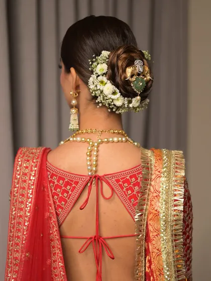 A detailed view of a classic bridal bun, intricately woven and adorned with a ring of fresh white flowers and a jeweled pin. This hairstyle is both traditional and incredibly chic.
