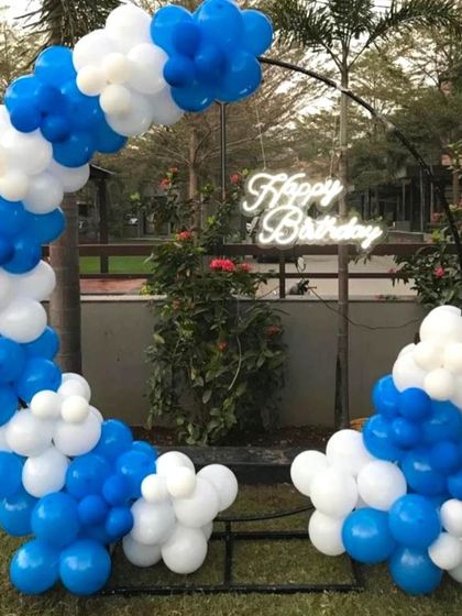 A simple and clean balloon arch decoration in blue and white, perfect for an outdoor birthday party. The half-ring design is modern and allows the natural background to be part of the decor.