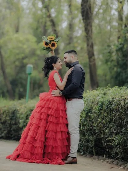 A beautiful pose during a pre-wedding session in a Pune garden. The woman's vibrant red dress stands out against the green foliage, creating a visually stunning and romantic photograph.