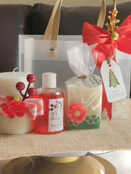 A simple yet elegant Christmas gift bag containing a decorated pillar candle, a floral soap, and a berry-scented body wash.