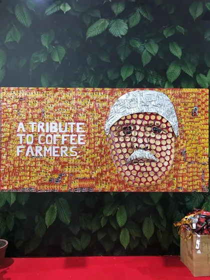 As a tribute to coffee farmers, this portrait was created live at the World Coffee Conference using waste from the Nescafé stall. The face is formed from used paper cups, and the background is a mosaic of empty coffee sachets contributed by visitors, making it a truly collaborative and sustainable piece.
