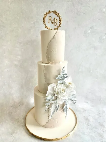 A winter-themed wedding cake with a touch of sparkle. This three-tiered design has a subtle marbled texture and is decorated with beautiful white sugar flowers and silver-dusted leaves for a frosty, elegant look.