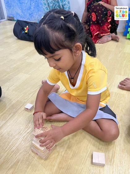 Concentration and determination. This child is carefully stacking wooden blocks, a simple activity that builds fine motor skills, spatial awareness, and the ability to focus on a task.