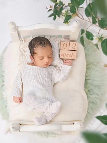This two-week-old baby is peacefully asleep on a tiny bed, framed by greenery. The wooden blocks mark this precious milestone in a simple, beautiful way.