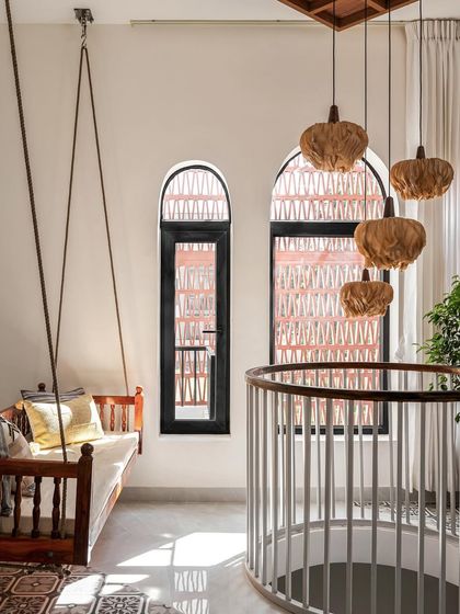 The first-floor living area features a traditional wooden swing set against arched windows with jali-inspired grills, blending multiple traditional elements in a light-filled, modern space.