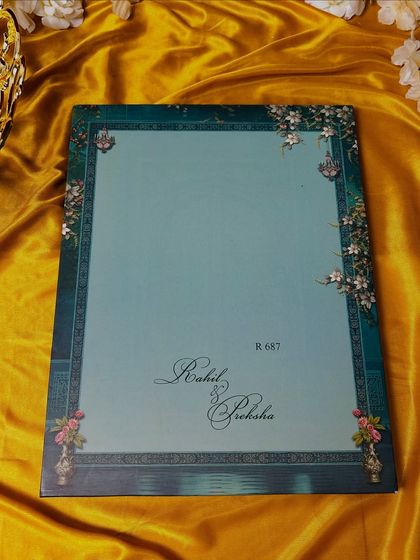 A clean and elegant invitation cover in a soft teal, with the couple's names in a beautiful script, framed by a traditional border.