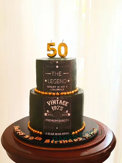 "The Man, The Myth, The Legend." A two-tier vintage-themed cake for a 50th birthday, designed to look like a classic whiskey label. The dark color and gold details give it a distinguished look.