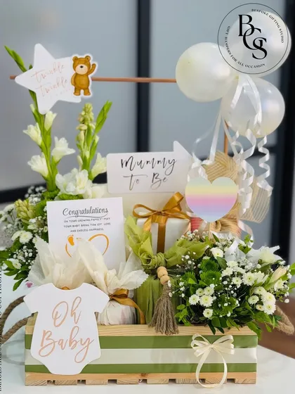 A beautiful "Mummy to Be" hamper designed to pamper the expectant mother. This wooden crate is filled with fresh white flowers, relaxing essentials, and cute baby-themed decorations like an "Oh Baby" onesie cutout.