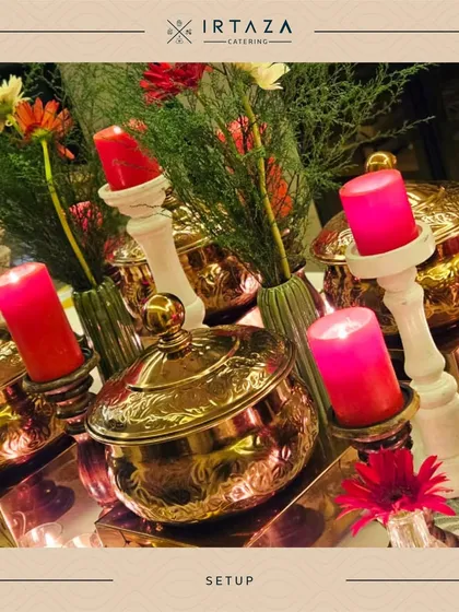 A vibrant and colorful setup featuring hammered copper pots, bright pink candles, and fresh flowers. This lively arrangement is perfect for festive occasions like sangeets or birthday parties.