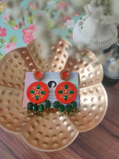 These hand-painted earrings feature a vibrant orange base with green zardozi embroidery and bead drops. They are perfect for adding a pop of color to your look.