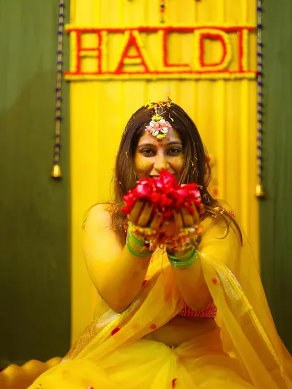 A playful and colorful Haldi photo, with the bride holding a handful of bright red flower petals.