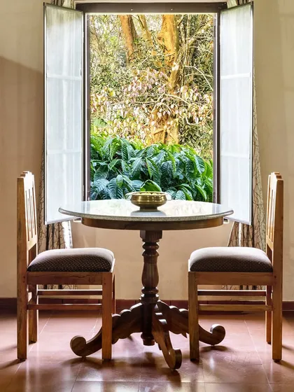 A small dining table for two, perfectly positioned in front of a window that opens to a lush green view. This intimate setting captures a romantic and peaceful moment at the resort.