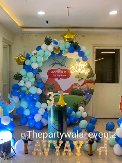 A cool dinosaur theme with a blue and green color scheme. The balloon arch is decorated with star-shaped foil balloons and dinosaur cutouts.