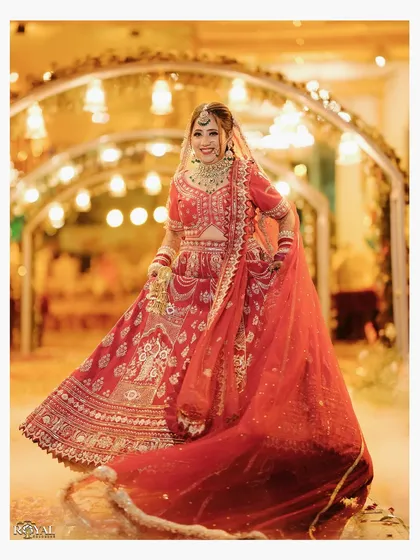 A radiant portrait of the bride twirling in her red wedding lehenga, captured under a beautifully lit archway.