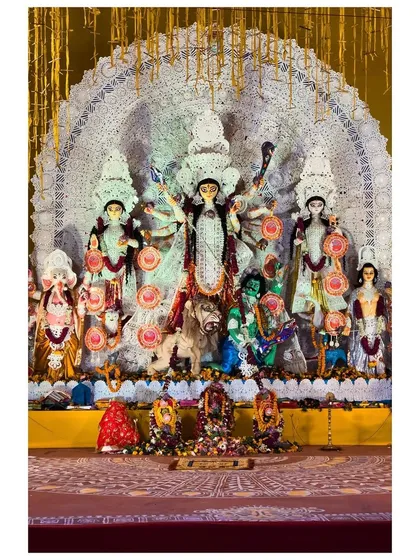A traditional Durga idol with a large, decorative 'Chalchitra' (backdrop) at a community pandal.