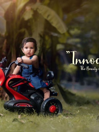 Innocence unveiled. A cool toddler in denim overalls sits confidently on his red toy motorcycle.