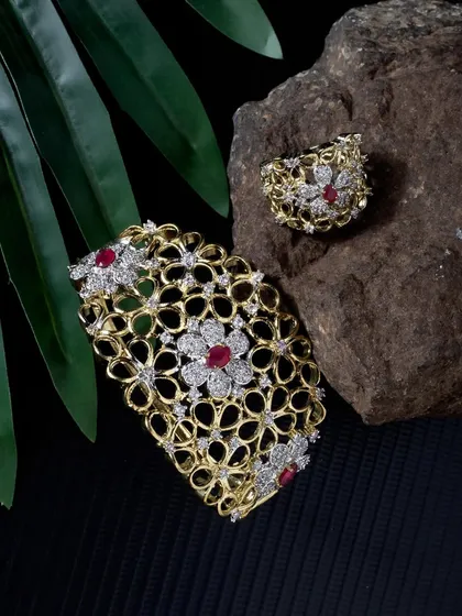 A stunning floral-design bracelet and ring set with ruby and diamond details. The lighting is carefully controlled to capture the sparkle of the stones against a natural, textured background.