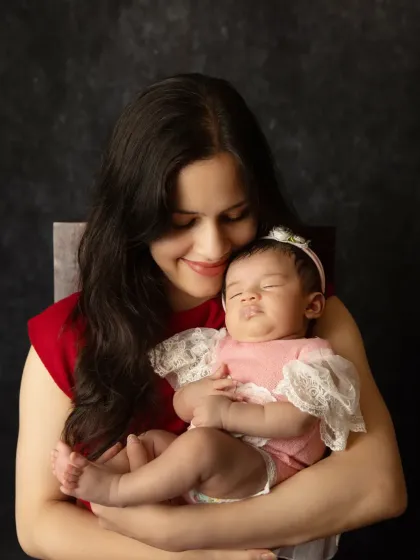 A mother gazes lovingly at her peacefully sleeping newborn, cradled securely in her arms during their first photoshoot together.
