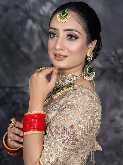 A beautiful reception or engagement look. The combination of a golden-beige lehenga with emerald green jewelry is perfectly complemented by soft glam makeup, focusing on luminous skin and defined eyes.
