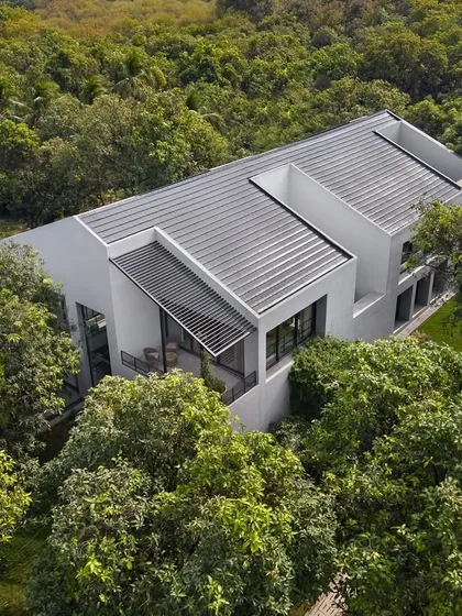 The clean, white monolithic form of the house contrasts with the organic texture of the surrounding trees. The roofline is punctuated by openings for the open-to-sky courtyards that bring light into the home's core.