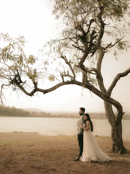A couple finding a quiet moment under a sprawling tree by the lake. This wide shot emphasizes the beauty of nature as a setting for your love story.