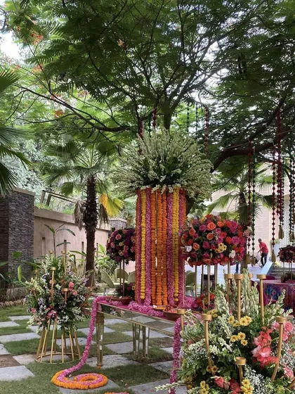 For grander celebrations at home, we specialize in creating lavish floral installations. This garden setup features towering arrangements of marigolds and lush bouquets of roses and mixed florals, demonstrating our expertise in large scale floral artistry. We use mirrored tables and elegant stands to add a touch of glamour to the outdoor space.