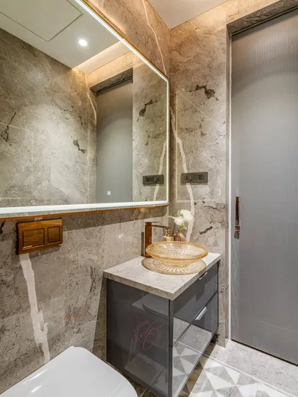 This bathroom uses a sophisticated palette of grey marble with brushed gold fixtures. The textured glass basin and large, back-lit mirror enhance both the aesthetics and the utility of the space.