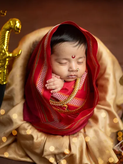 This shot highlights the beautiful texture of the traditional saree wrap and the golden jewelry against the baby's soft skin.
