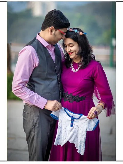 The couple holds up a tiny baby outfit, a sweet symbol of the little one they are eagerly awaiting.